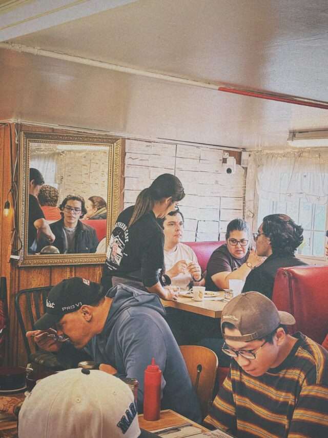 Group of people dining at a retro-style cafe, chatting and eating around a long table.